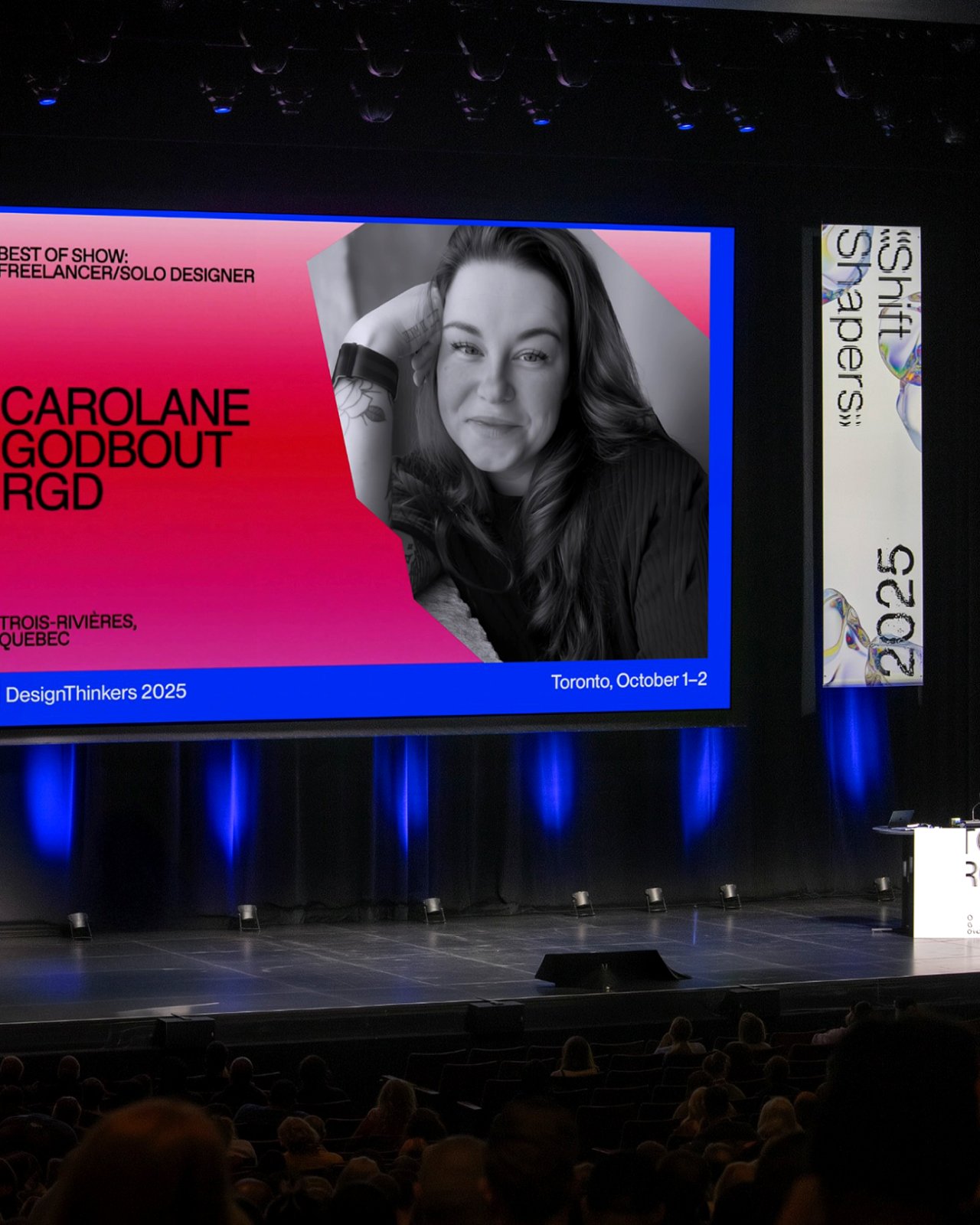 Large stage screen at DesignThinkers conference displaying a winner profile with the RGD jagged brand framing.