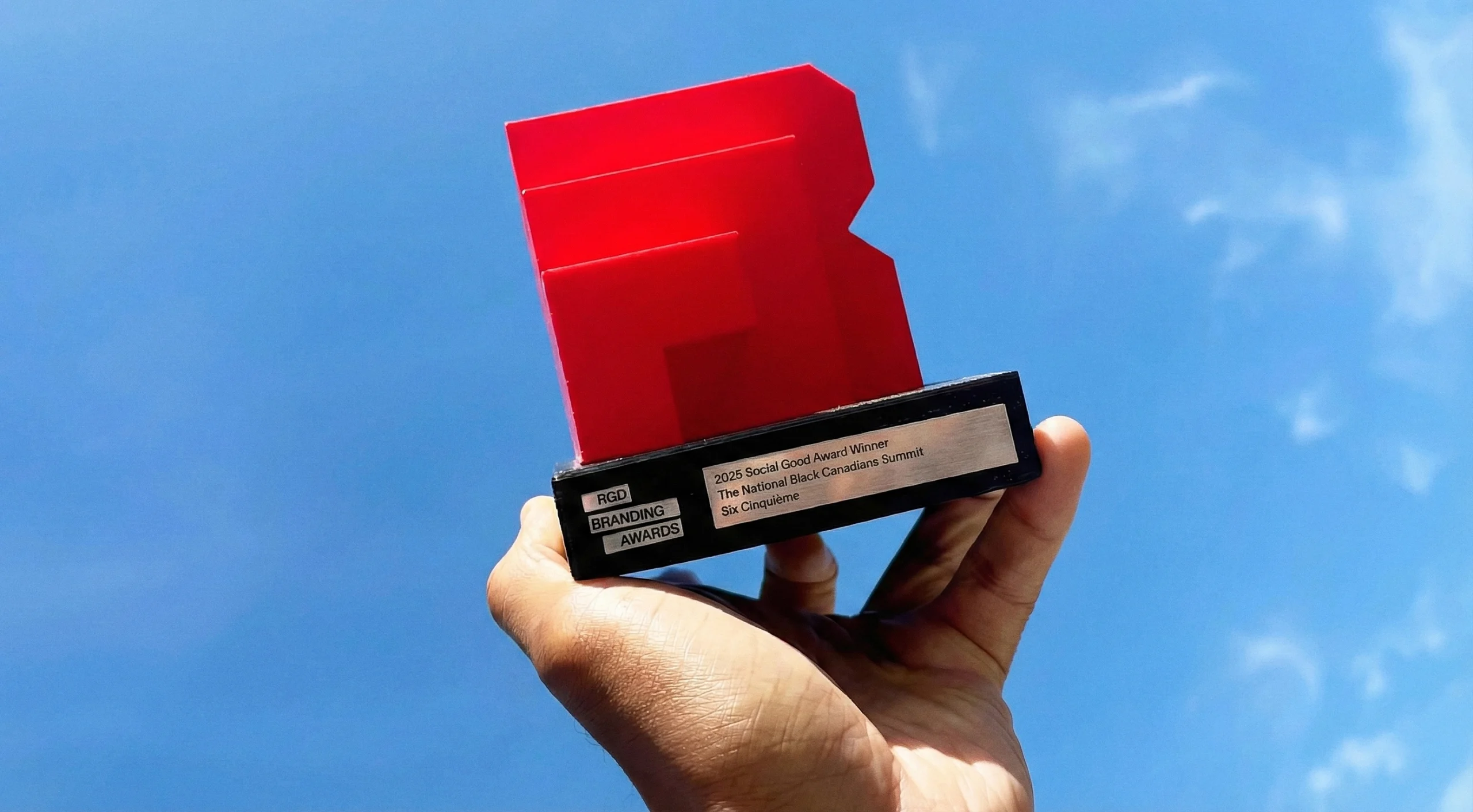 Hand holding the custom RGD Branding Award trophy, a translucent ruby red 3D "R" shape on a black base.
