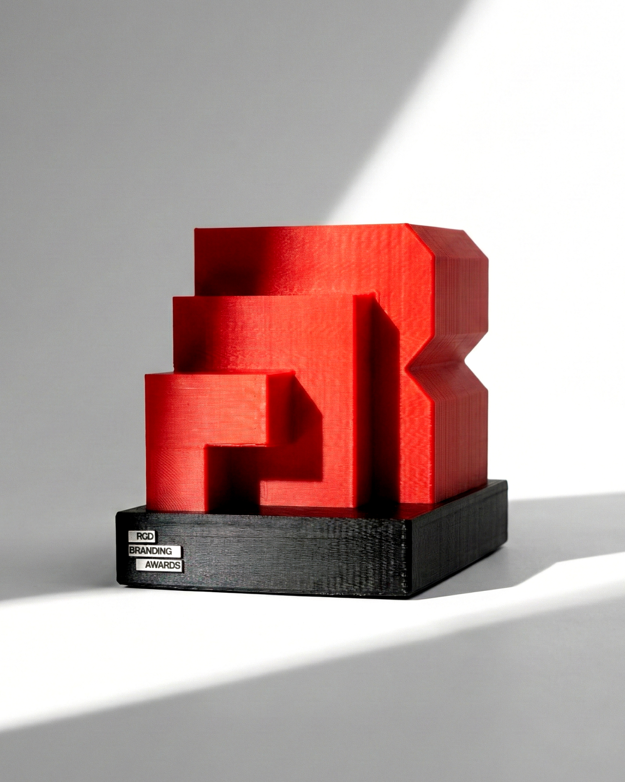 Studio product shot of the red RGD Branding Awards trophy showing the 3D layered construction and black plinth.