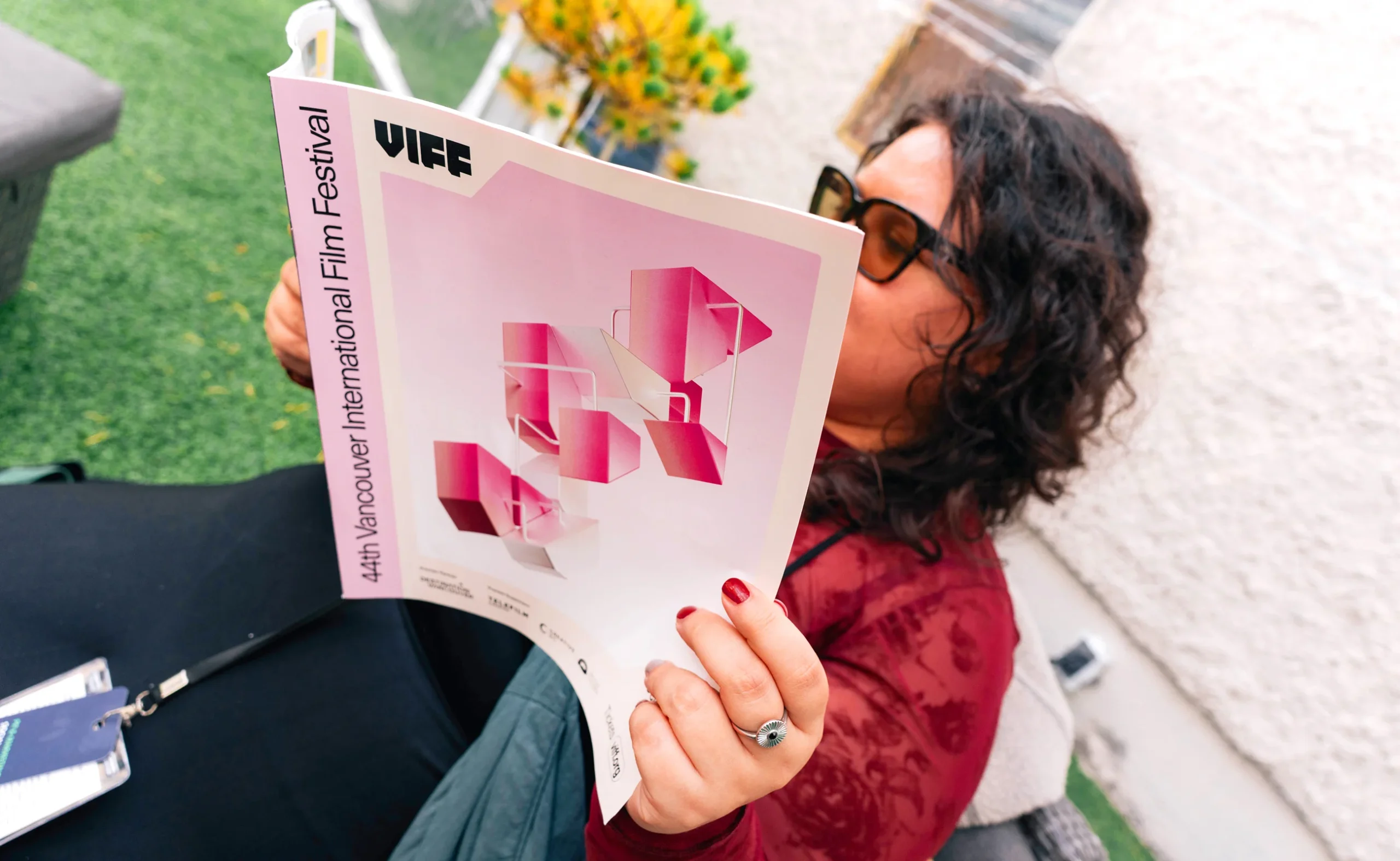 A person reading the official VIFF 2025 printed guidebook featuring pink 3D brand structures.