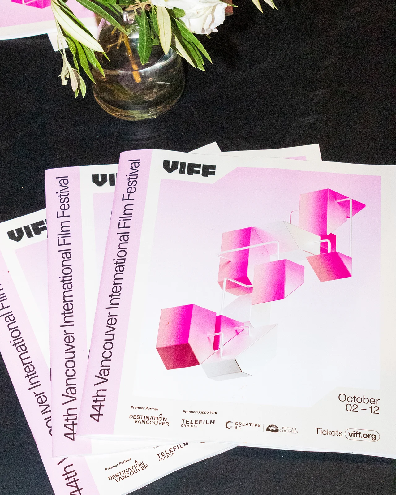Stack of printed festival guidebooks for VIFF 2025 showing modular 3D brand structures and optimistic colors.