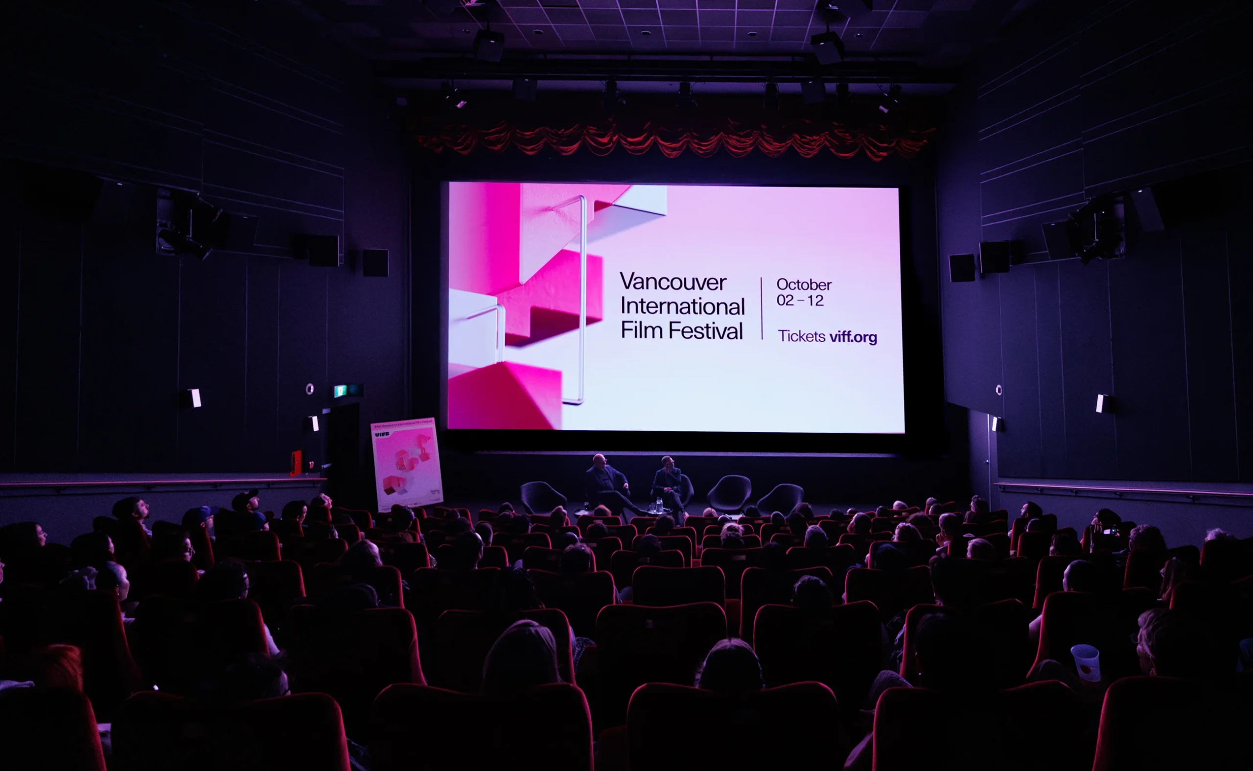 A large cinema screen displaying the pink 3D VIFF 2025 visual identity during a live presentation.