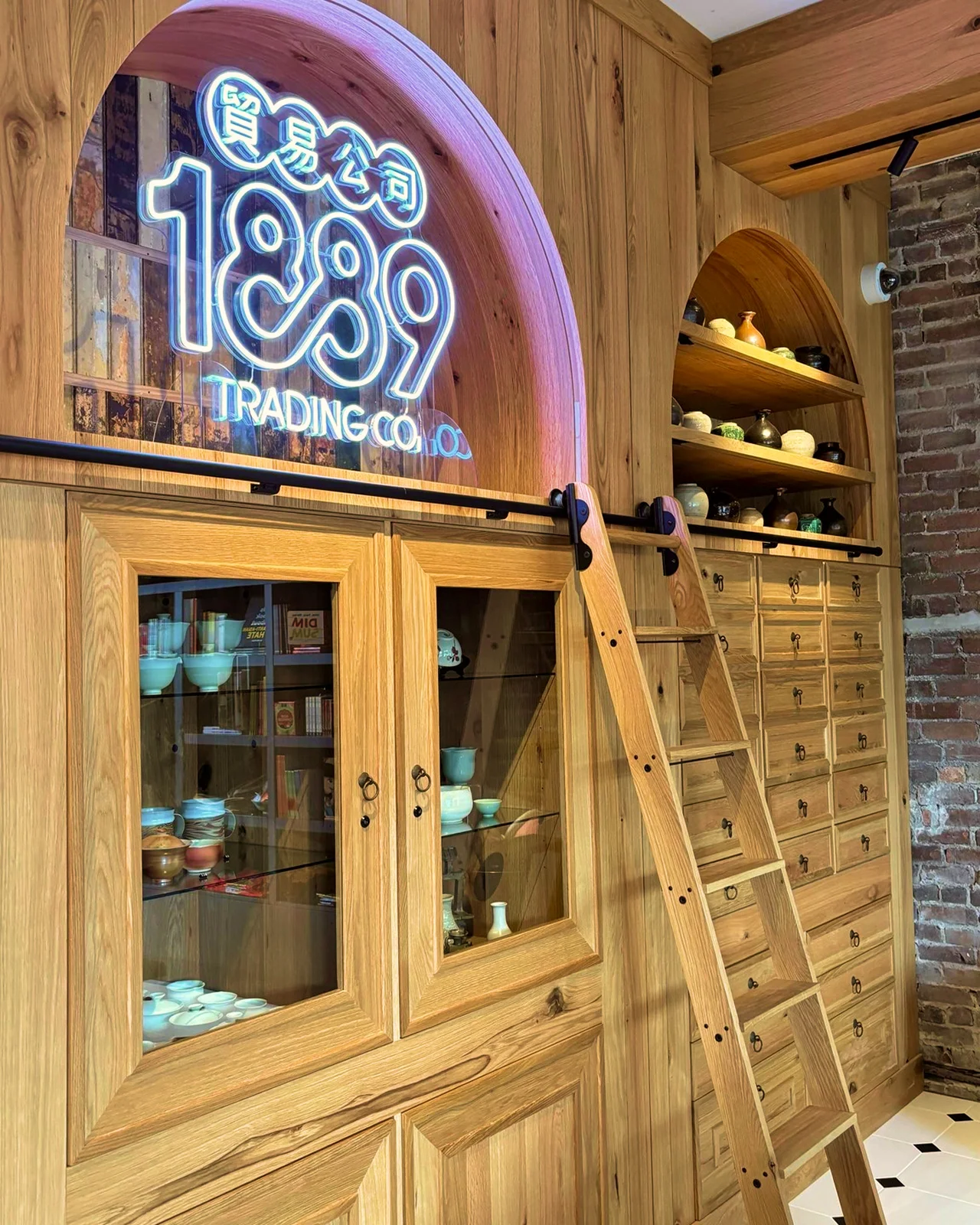 Modern retail interior with light wood cabinetry, apothecary drawers, and an arched neon 1889 Trading Co. logo.