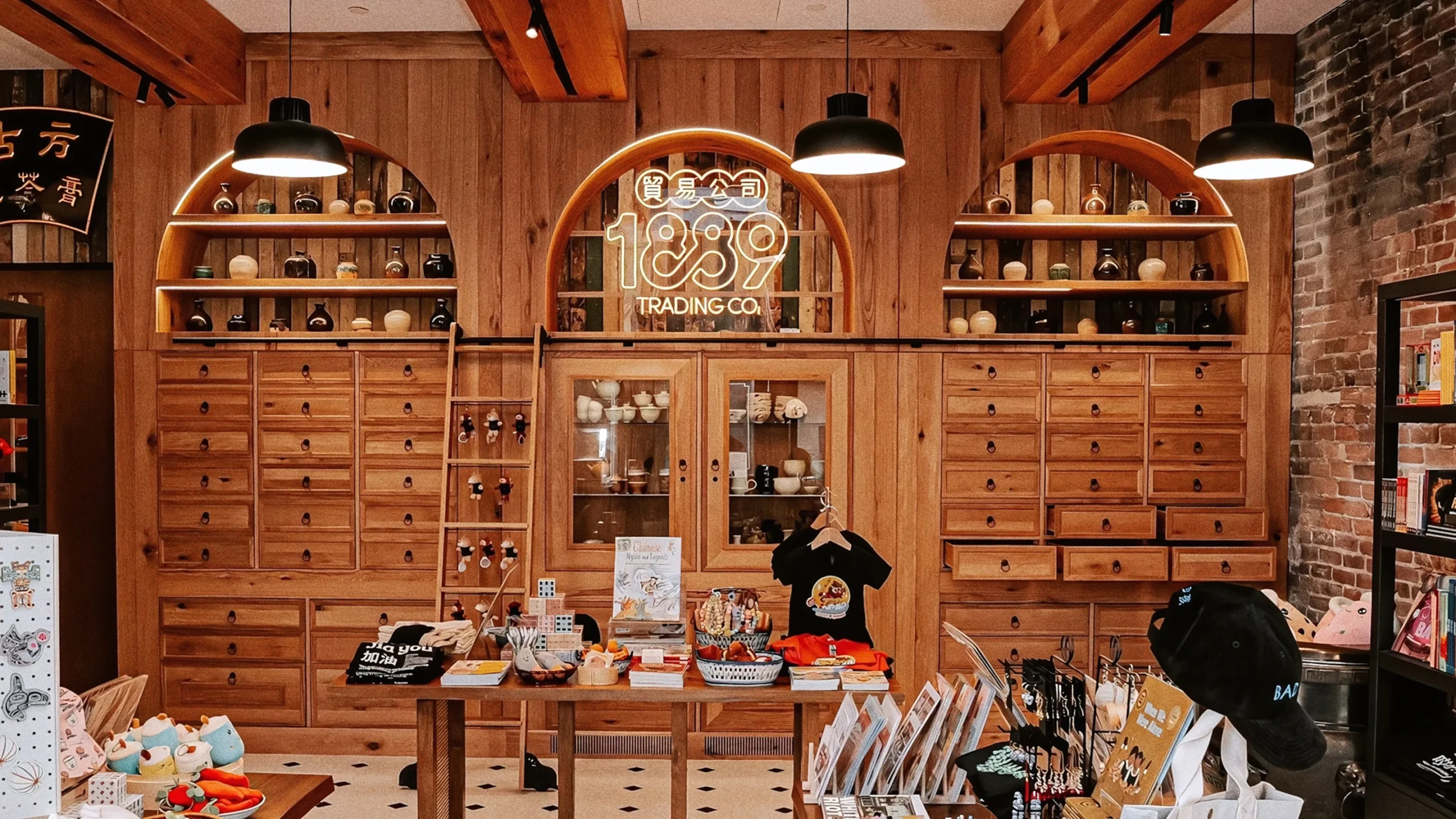 Modern retail interior with light wood cabinetry, apothecary drawers, and an arched neon 1889 Trading Co. logo.