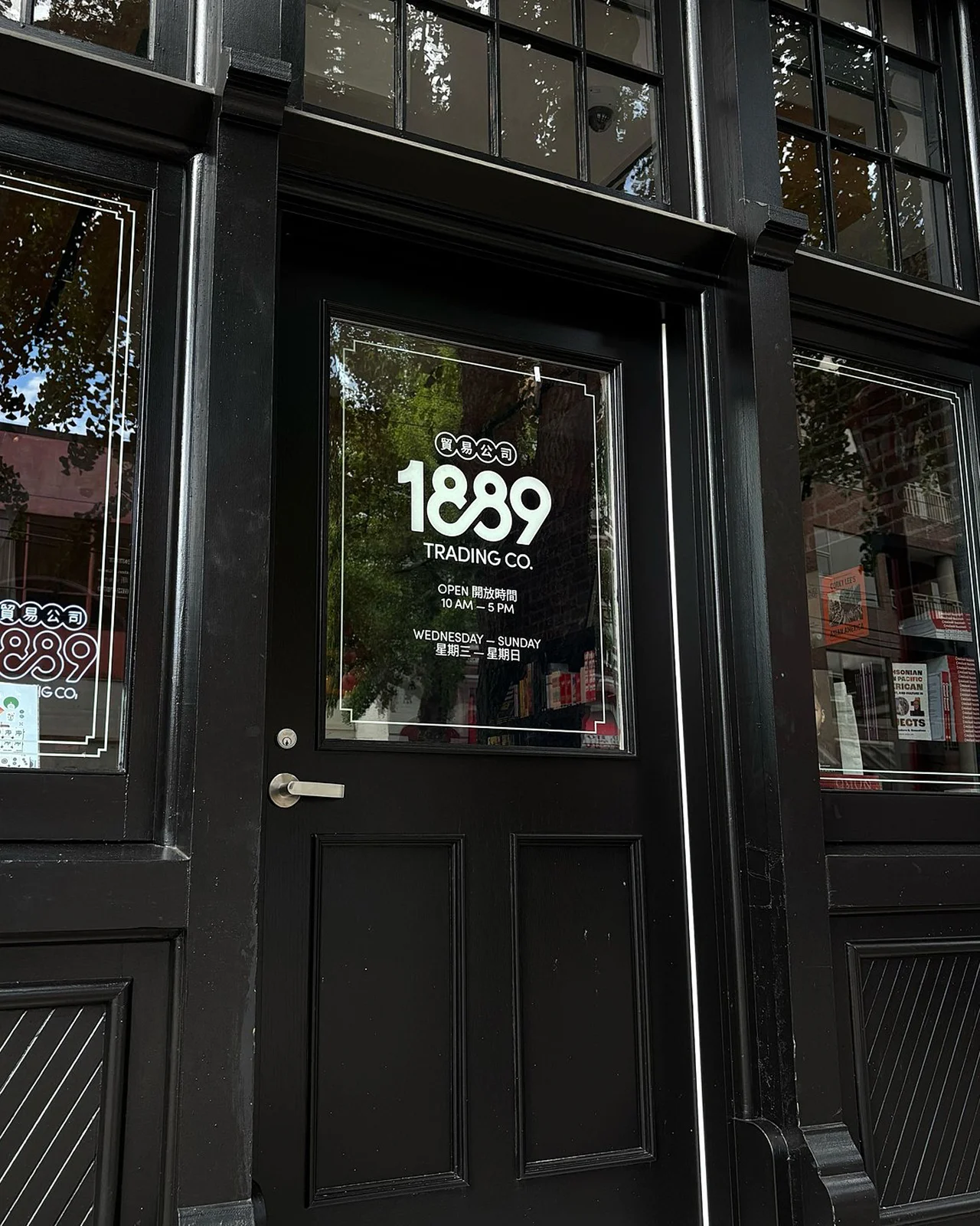 Modern retail interior with light wood cabinetry, apothecary drawers, and an arched neon 1889 Trading Co. logo.