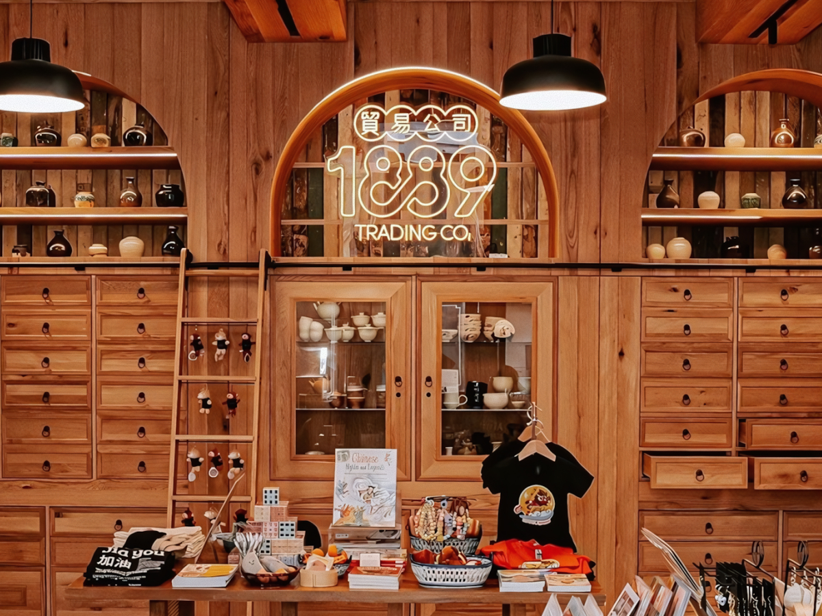 Modern retail interior with light wood cabinetry, apothecary drawers, and an arched neon 1889 Trading Co. logo.
